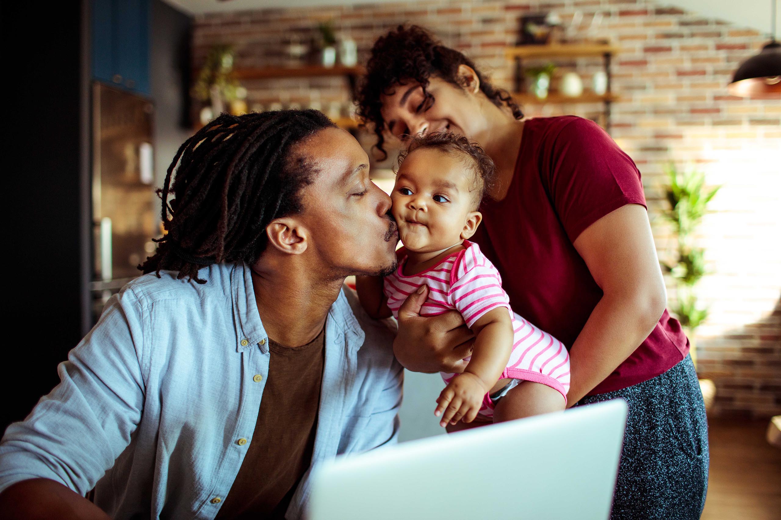 Photo of a dad kissing his baby while mom is holding her.